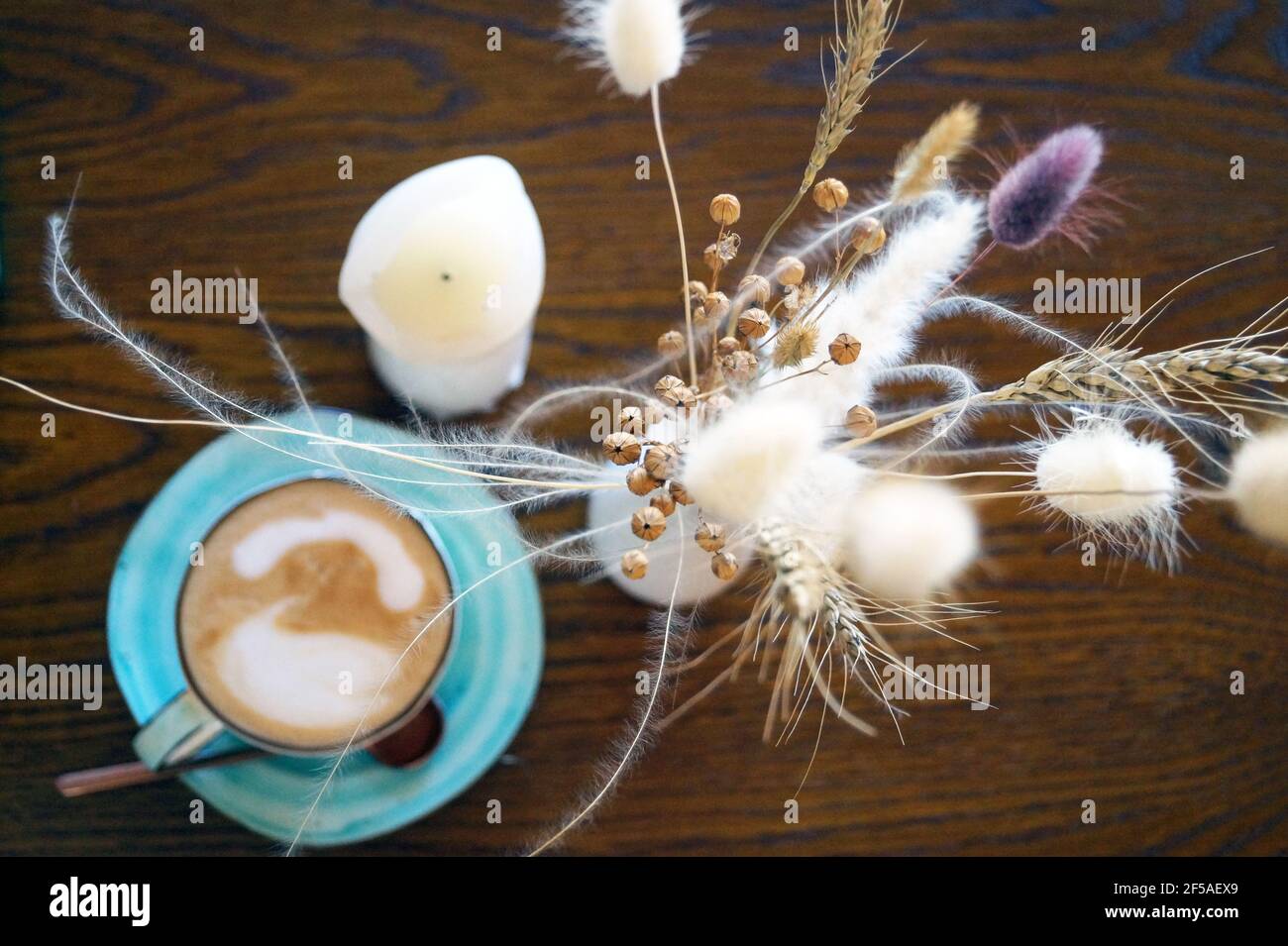 Trockene Blumen in einer Vase auf einem Tisch stehen neben Zu einer Tasse Kaffee ein Stockfoto