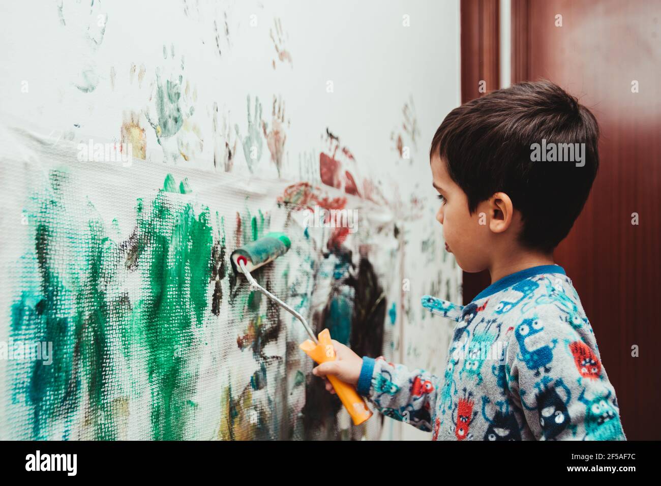 Kind spielt, um Farben an der Wand seines Hauses zu malen Mit Walze und Acrylfarbe Stockfoto