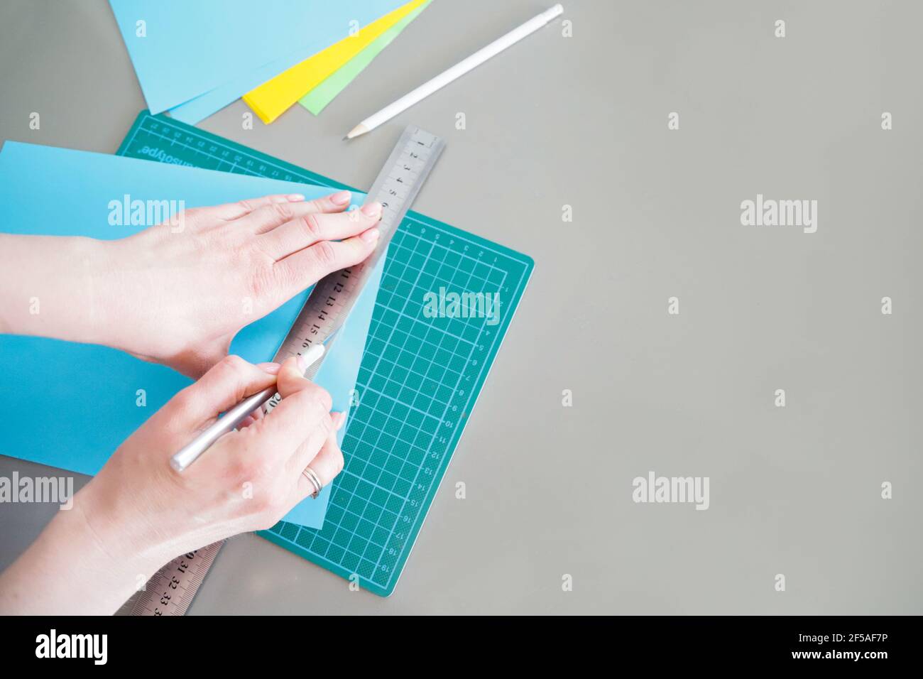 Frauenhände schneiden blaues Papier für eine Lektion von Postkarten. Der Stockfoto