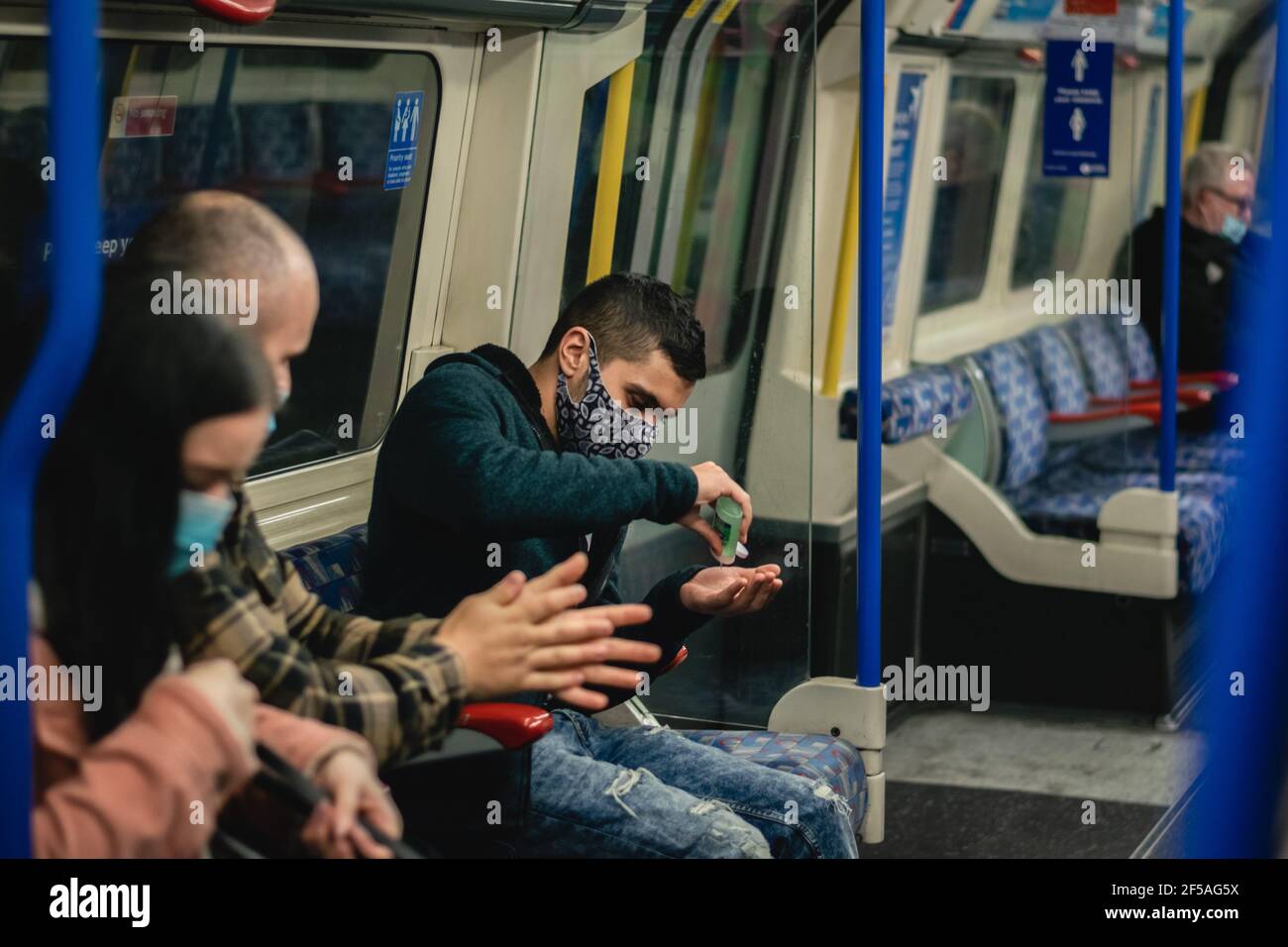 Junger Mann, der seine Hände desinfiziert, während er mit der U-Bahn/U-Bahn in London, England, reist Stockfoto