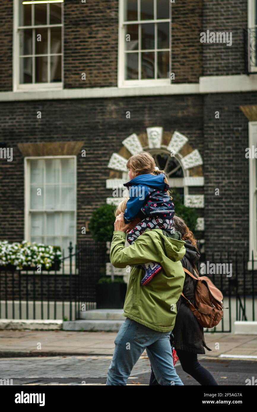 Vater trägt sein Kind auf der Schulter die Straße hinunter In London zusammen mit der Mutter des Kindes Stockfoto