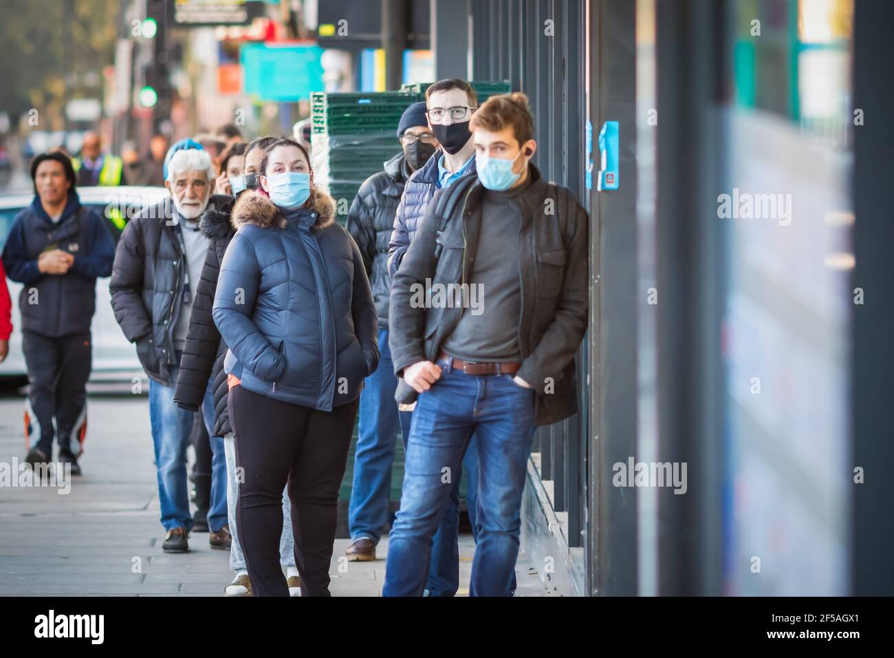 London, Großbritannien - 26. Februar 2021 - Kunden mit Gesichtsmasken, die während der COVID-19-Pandemie vor dem Laden anstehen Stockfoto