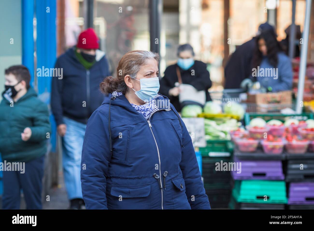 London, Großbritannien - 5. Februar 2021 - eine ältere Frau mit einer schützenden Gesichtsmaske, die an einem Markt für Outdoor-Produkte auf der Wood Green High Street vorbeikommt Stockfoto