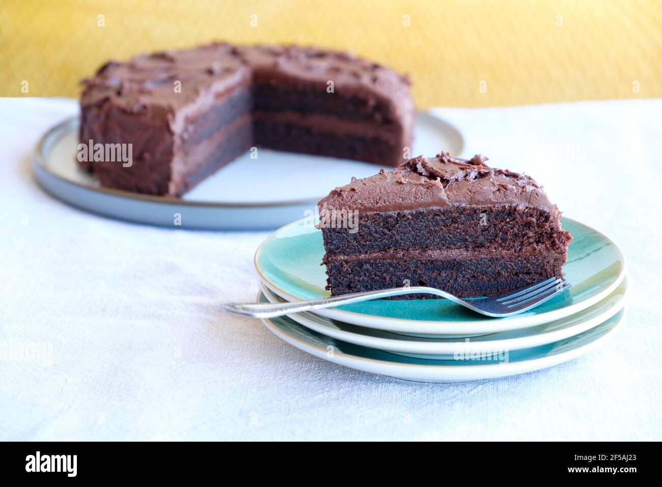 Ein Stück oder ein Teil des hausgemachten reichen, feuchten Schokoladenkuchen auf einem Teller. Die Tortenscheibe hat eine Schokoladencreme-Füllung und einen dicken Schokoladenüberzug Stockfoto