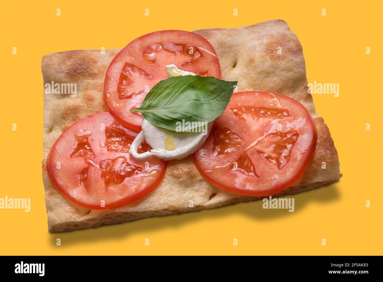 Scheibe ligurische Focaccia mit frischer Tomate, Mozzarella, Basilikumblatt und nativem Olivenöl extra - isoliert auf gelb, Draufsicht Stockfoto