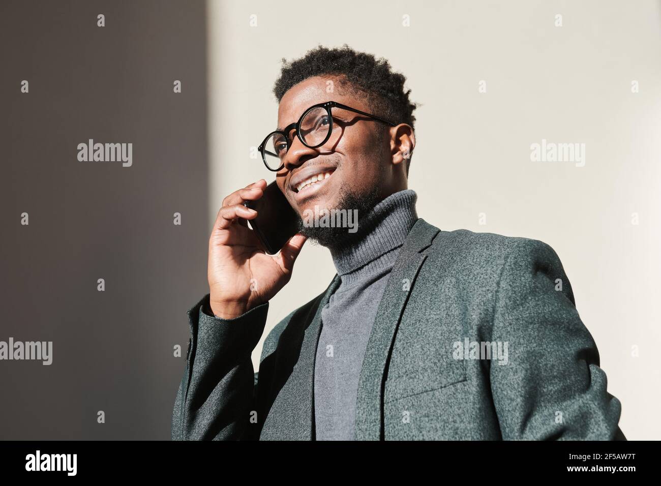 Afrikanischer junger Geschäftsmann in Brillen lächelnd, während er auf dem Handy spricht Telefon im Freien Stockfoto