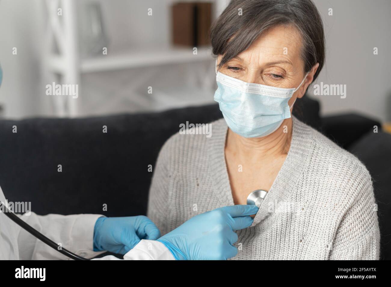 Krankenschwester Pflege von älteren weiblichen Patienten trägt Maske zu Hause während Coronavirus Pandemie, hört mit einem Stethoskop auf Herzfrequenz, Atemfrequenz. Arzttermin zu Hause Stockfoto