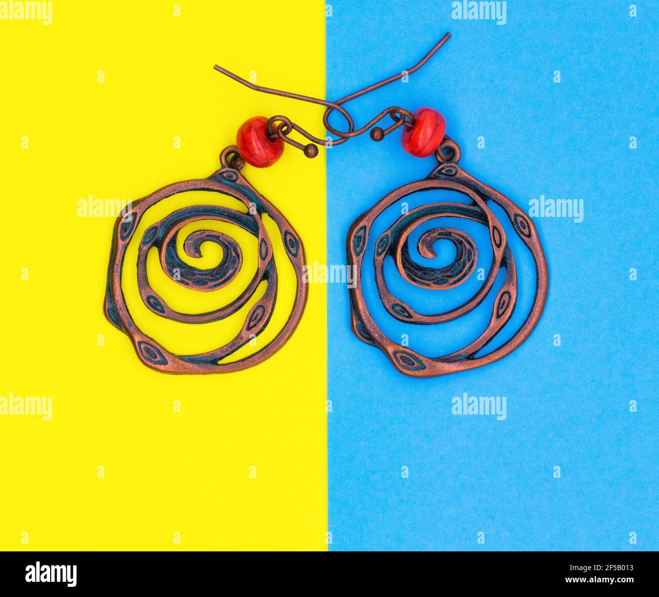 Ethnische Dekorationen auf farbigen Papierblättern. Ohrringe Ringe Amulette Perlen. Runde Ohrringe Aus Metall. Blauer und gelber Hintergrund. Stockfoto