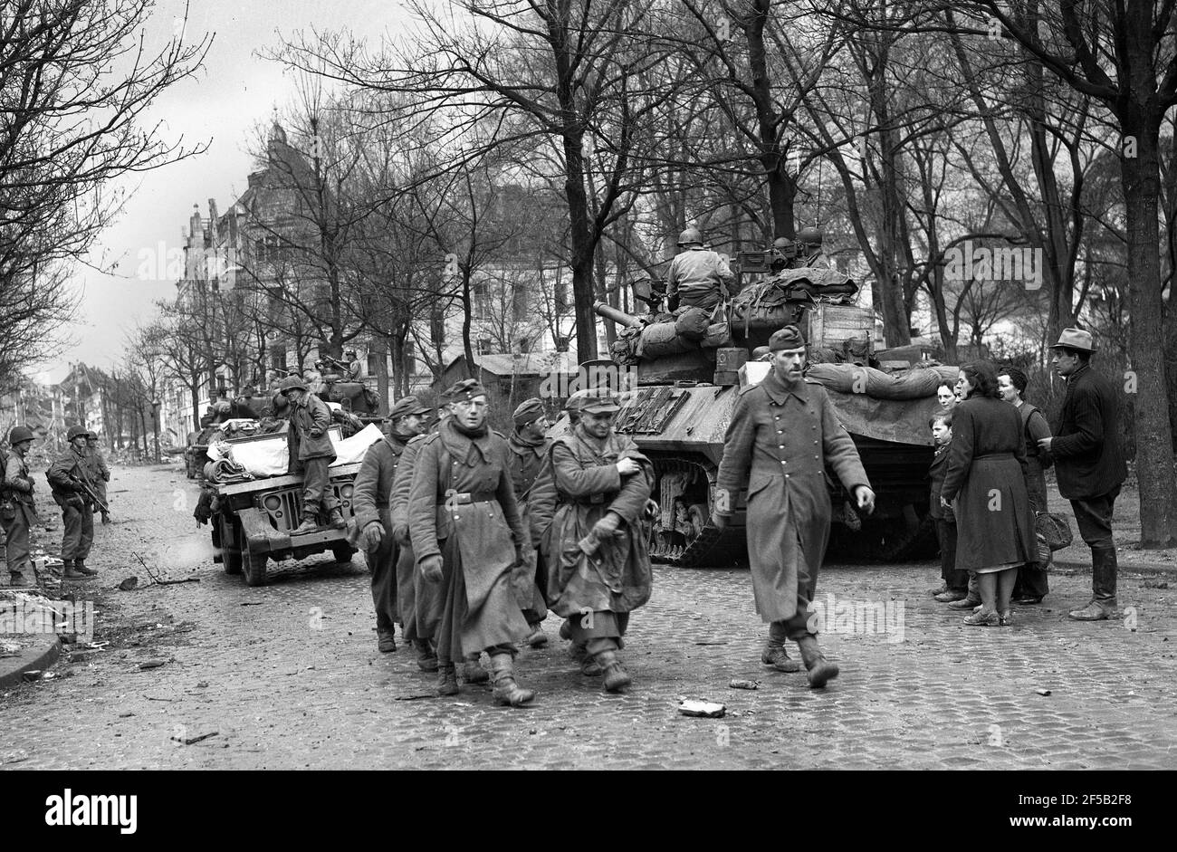 Köln, Deutschland 1945 amerikanische Truppen eskortieren gefangene deutsche Soldaten, nachdem sie sich während des Zweiten Weltkriegs, nach schweren Bombenangriffen auf die Stadt, von Einheimischen beobachtet, ergeben hatten. Zweiter Weltkrieg. deutsche Niederlage alliierter Sieg Deutschland 1940er Jahre Kapitulation Europa Europäische Geschichte Zerstörung Stockfoto