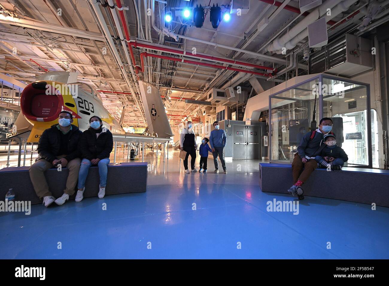 New York, USA. März 2021, 25th. Eine Familie schaut sich einen projizierten Dokumentarfilm im Hangardeck des Intrepid Sea, Air & Space Museums an, der heute nach einem Jahr wegen der COVID-19 Pandemie für die Öffentlichkeit wieder geöffnet wird, New York, NY, 25. März 2021. Das schwimmende Museum, das an Manhattans West Side angedockt ist, wird die Kapazität auf 25% begrenzen, den Eintritt zeitlich eingrenzen und Gesichtsbedeckung und soziale Distanzierung erfordern. (Foto von Anthony Behar/Sipa USA) Quelle: SIPA USA/Alamy Live News Stockfoto