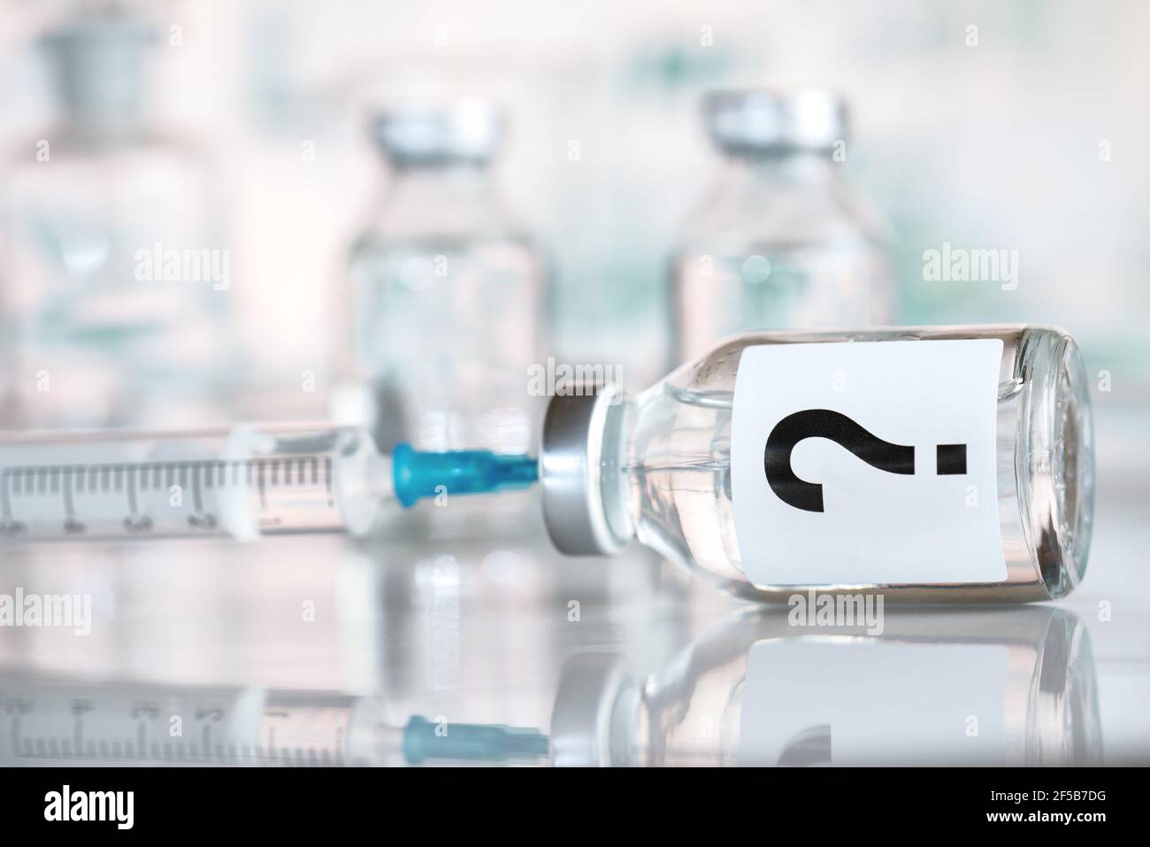 Impfstoffflasche mit hypodermischer Spritzennadel innen, Fragezeichen auf Etikett, Hintergrund der verschwommenen Fläschchen Stockfoto