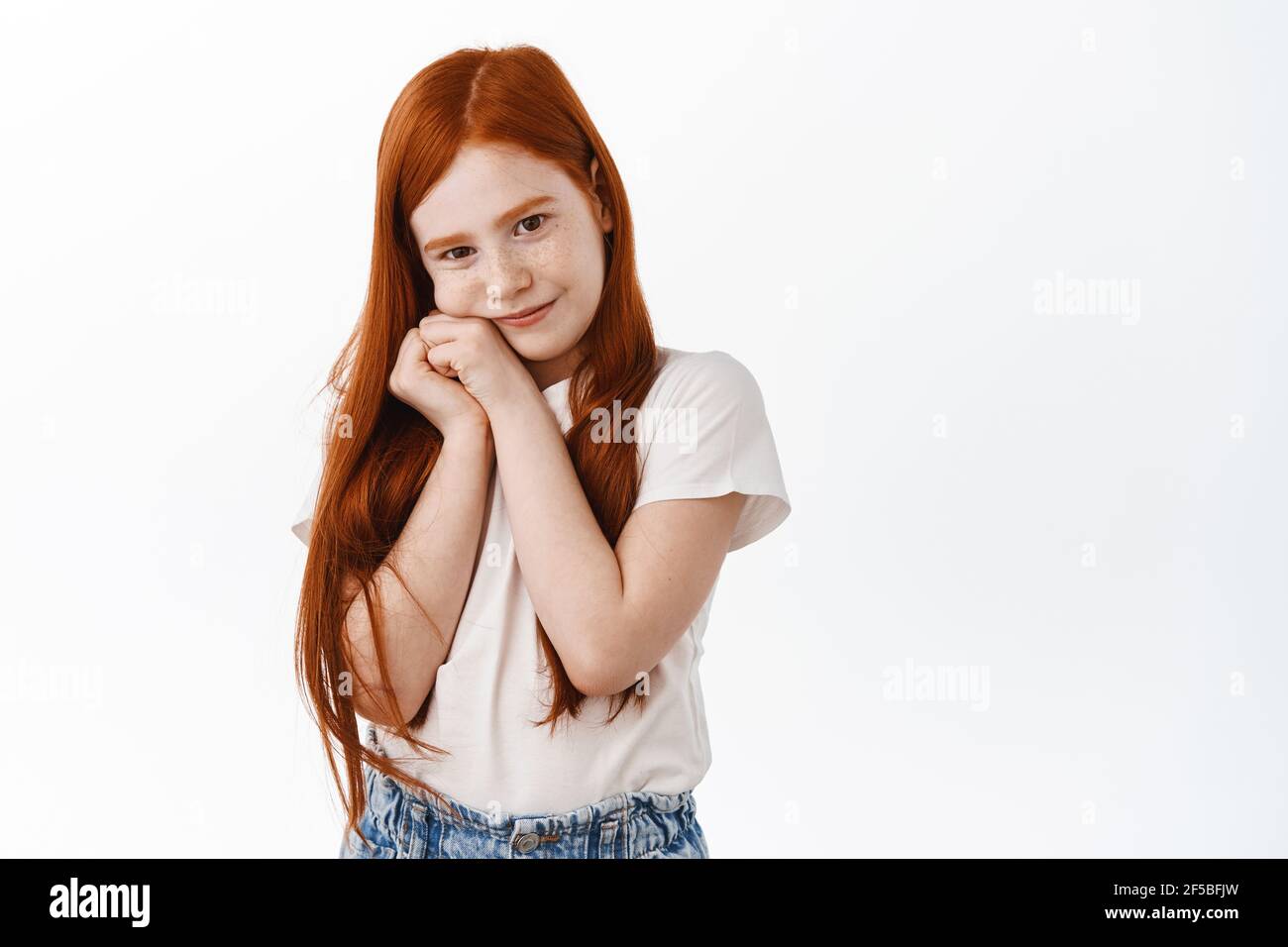 Schöne kleine Rotschopf Mädchen mit Sommersprossen und langen Ingwer Haar, suchen liebenswert und niedlich in der Kamera, hält die Hände in der Nähe Gesicht in dumme Pose, Tagträumen Stockfoto