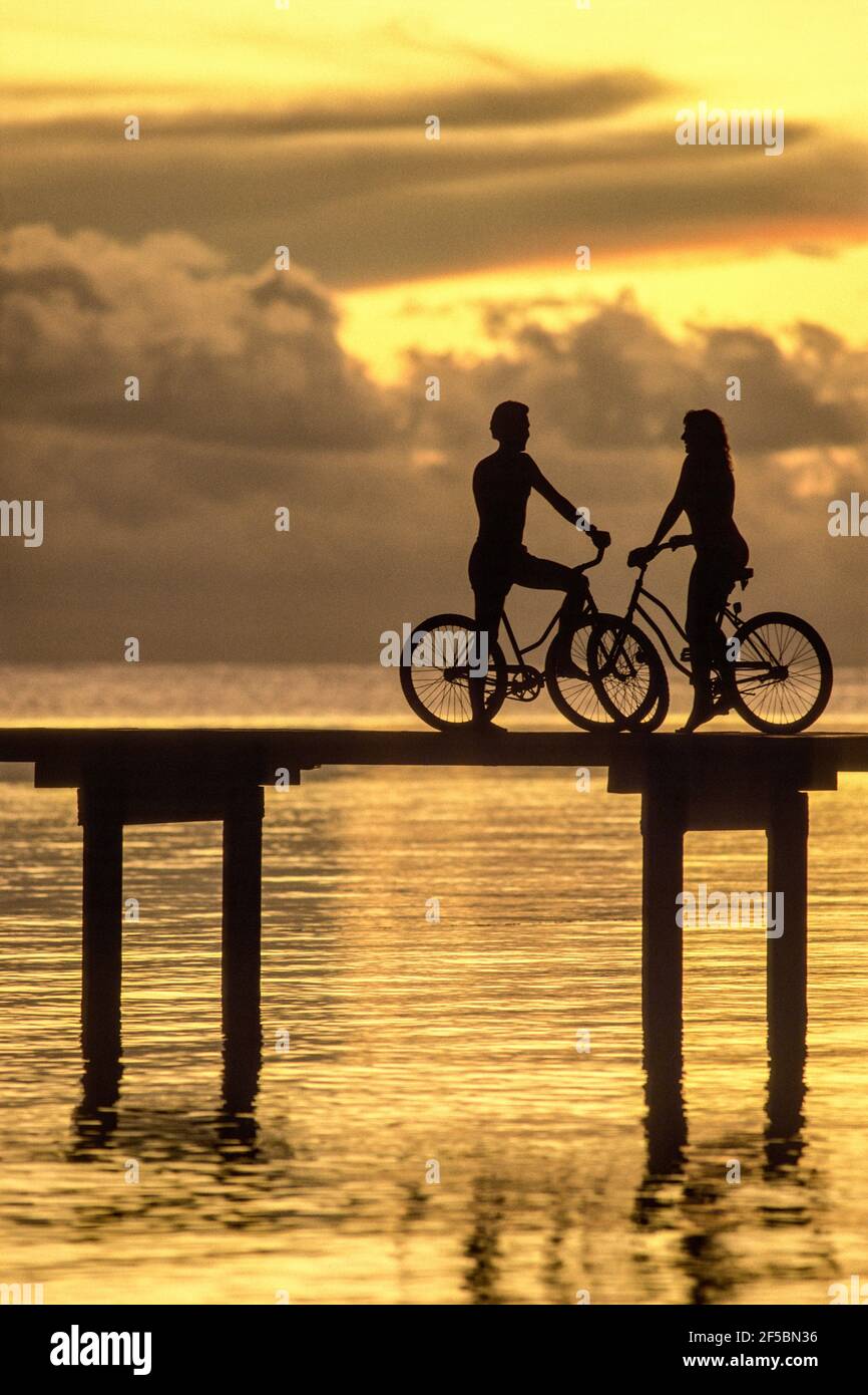 Mann und Frau auf Fahrrädern, Silhouetten gegen Sonnenuntergang in den Tropen Stockfoto