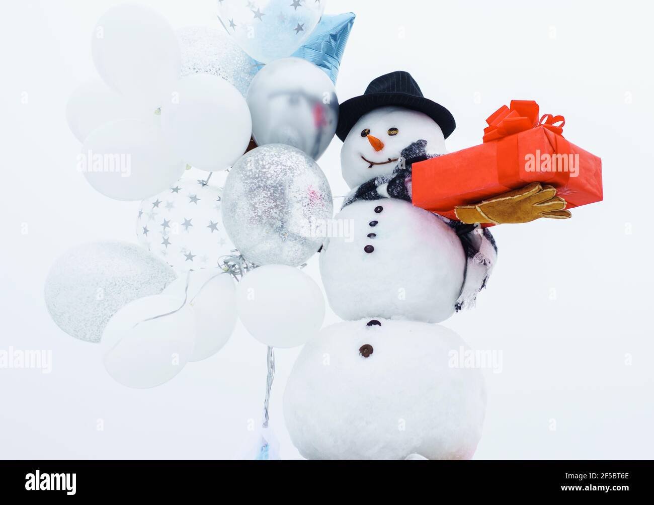 Frohe Winterzeit. Schneemann mit Ballons und Geschenk. Schneemann in Hut, Schal, Handschuhe. Stockfoto
