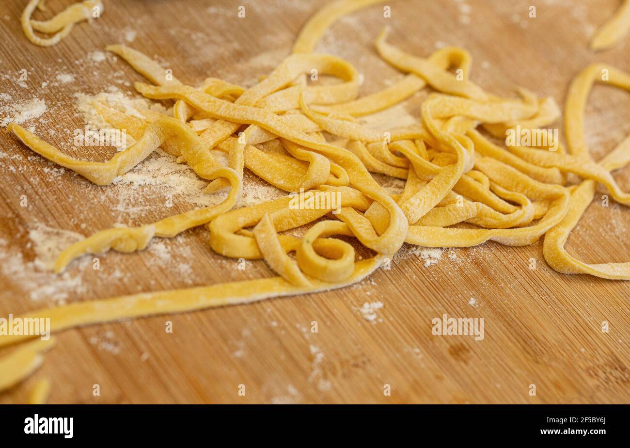 Italienische hausgemachte rohe, ungekochte Pasta-Tagliatelle mit Mehl auf Holzbrett. Stockfoto