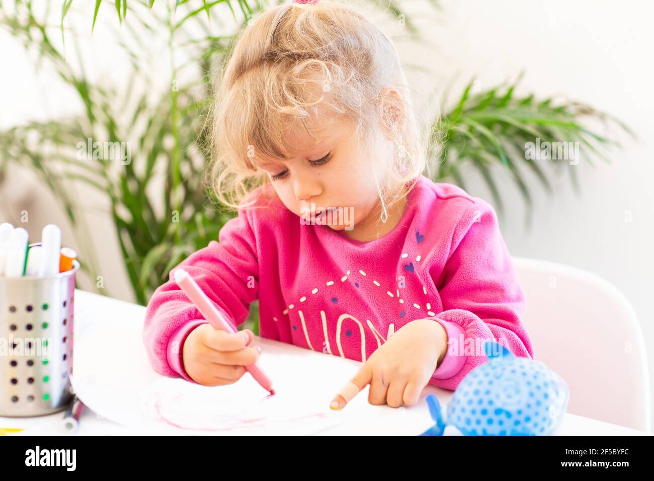 Unter Quarantäne Spaß. Kleines Mädchen, das während des Coronavirus-Ausbruchs malte und Hausaufgaben machte. Lebensstil unter Corona-Virus. Stockfoto