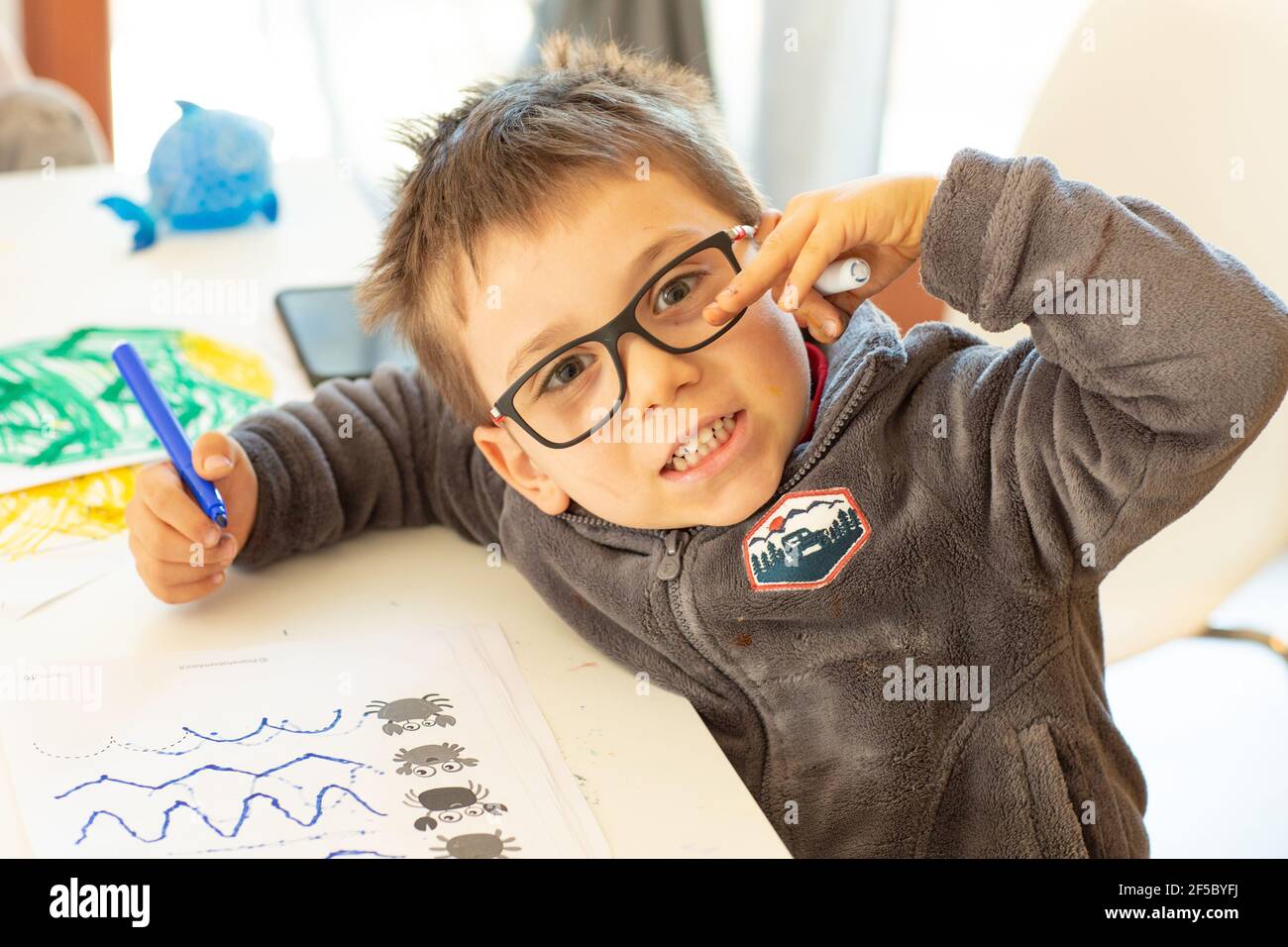 Unter Quarantäne Spaß. Kleiner Junge, der während des Coronavirus-Ausbruchs malte und Hausaufgaben machte. Lebensstil unter Corona-Virus. Stockfoto