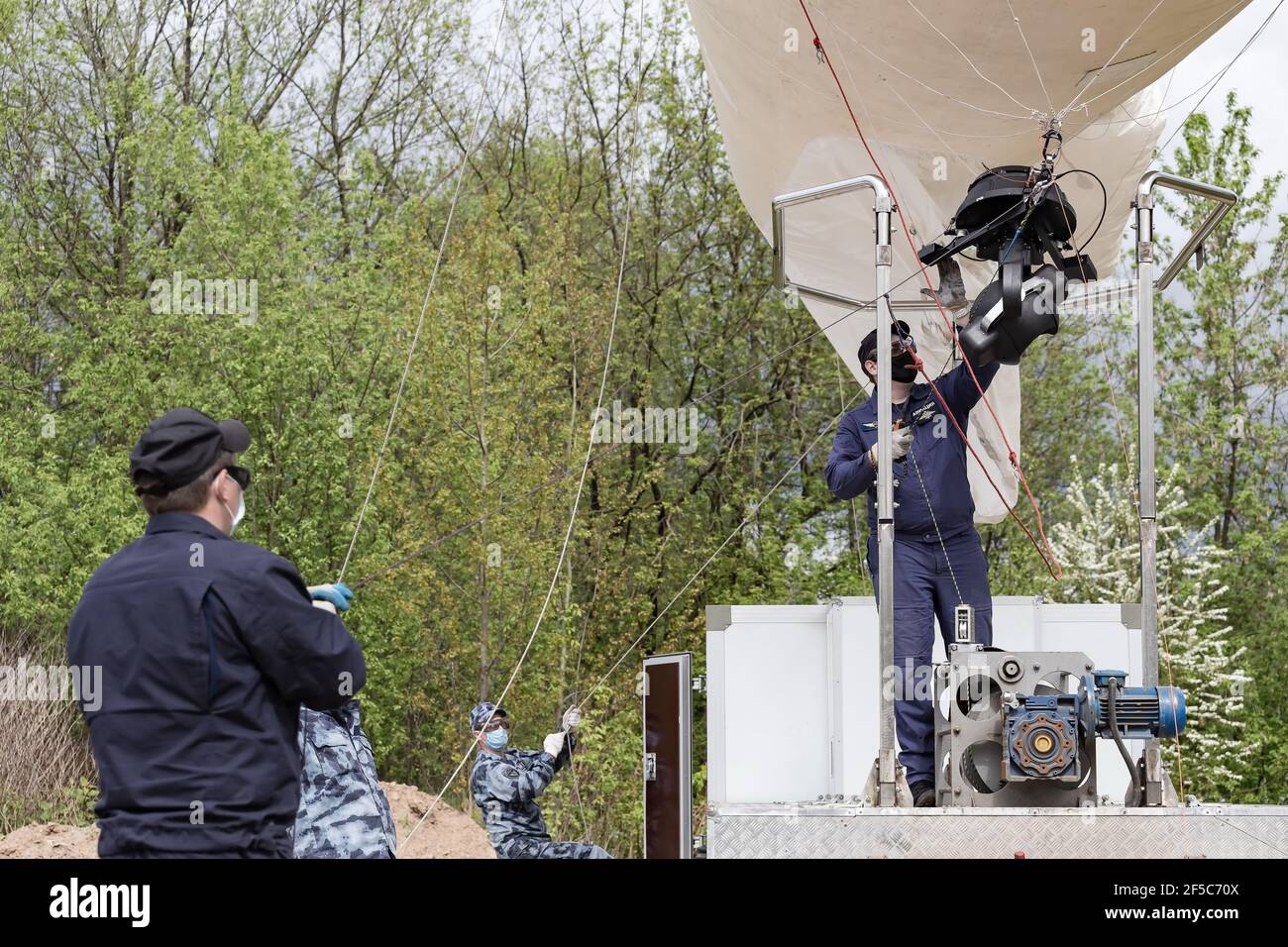 Spezialisten, die die Seile des Ballons am Boden strecken.Mitarbeiter von Rosgvardia mit dem OKO Videoüberwachungssystem (oder High-Altitude Video Surveillance System), das auf einem Ballon platziert wurde, um nach Sperrverletzern zu suchen, sollte diese Technik die Ausbreitung des Coronavirus verhindern (Covid-19). Es wurde auch auf der Website der Abteilung berichtet. Stockfoto
