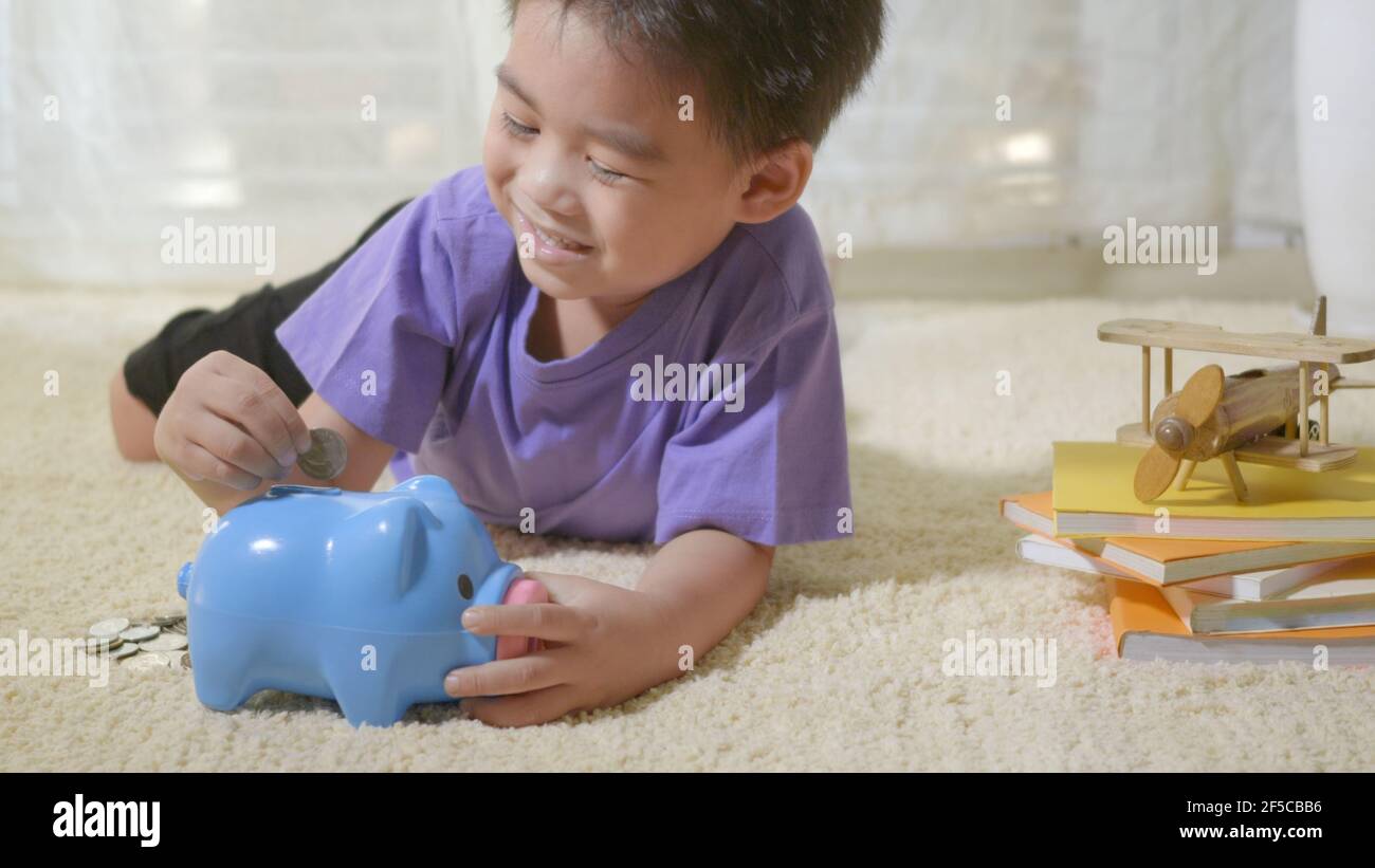 Glücklich asiatische Kind Junge Vorschule Putting Pin Geld Münzen in blau konfrontiert Ferkel slot. Kleines Kind Putting Münze in Sparschwein für das Sparen mit Haufen c Stockfoto