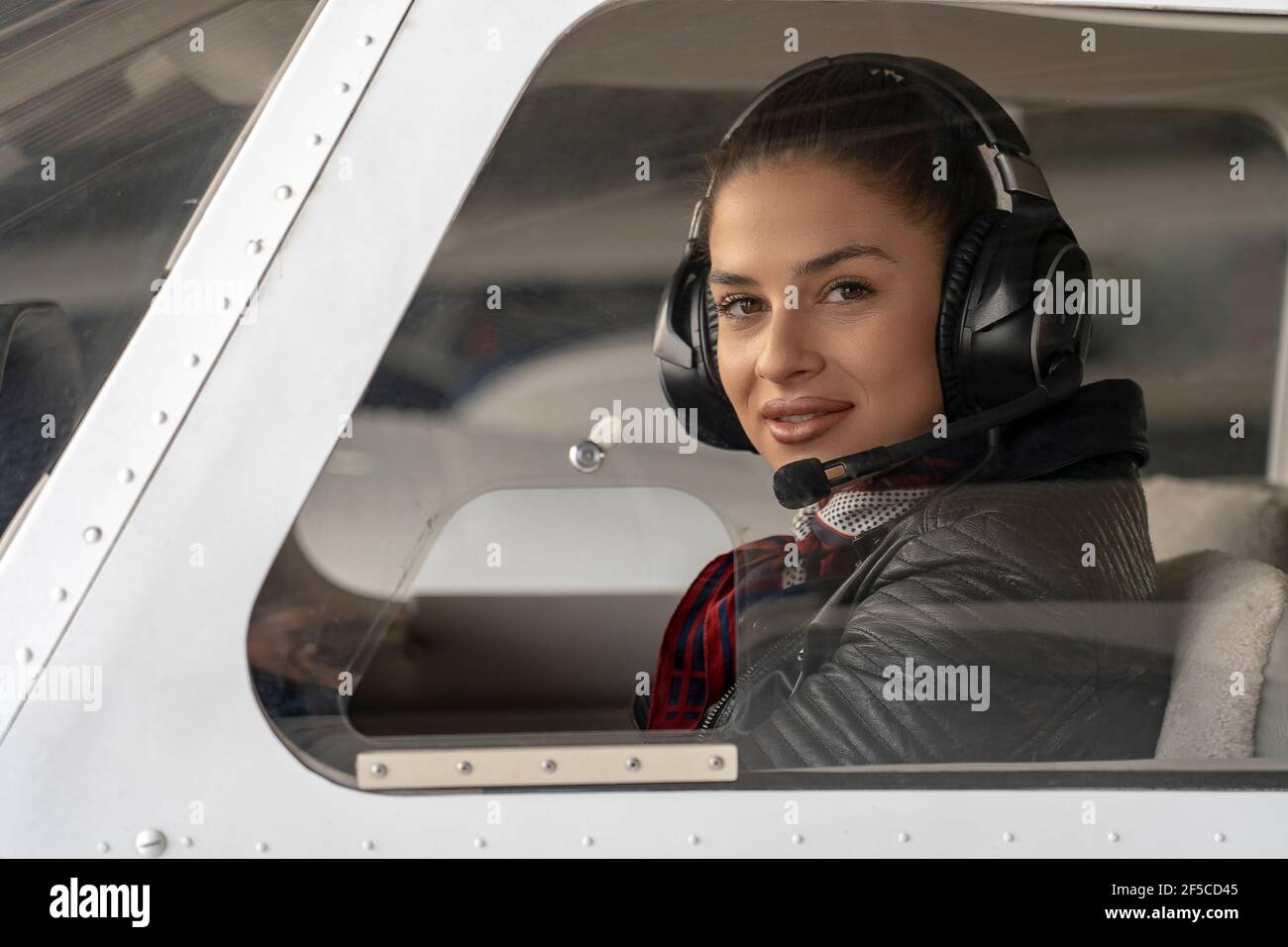 Porträt einer attraktiven jungen Frau Pilot mit Headset. Sie schaut durch das Cockpit-Fenster eines Privatflugzeugs auf die Kamera. Lächelnde Pilotin i Stockfoto