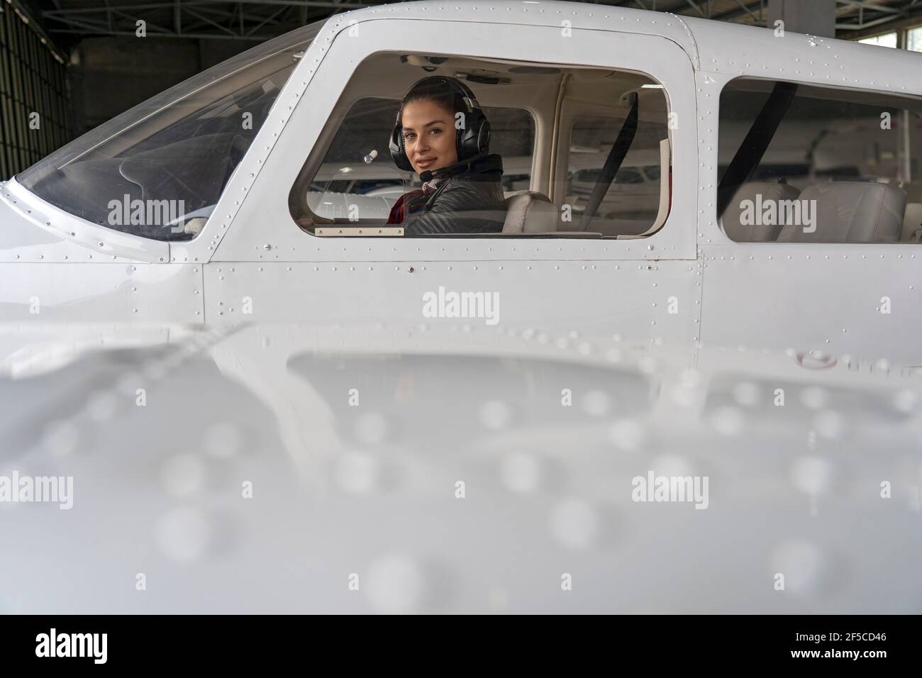 Porträt einer attraktiven jungen Frau Pilot mit Headset. Sie blickt durch das Cockpit-Fenster eines kleinen Flugzeugs auf die Kamera. Stockfoto