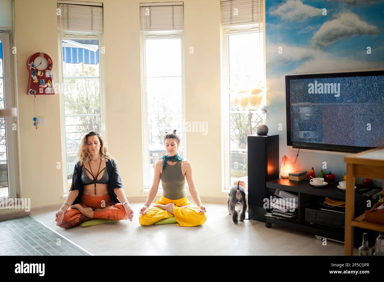 Zwei Freunde, die sich in einer Lotusposition in ihrem gemütlichen entspannen Wohnung und sich für einen Yoga-Unterricht zu Hause vorbereiten Stockfoto