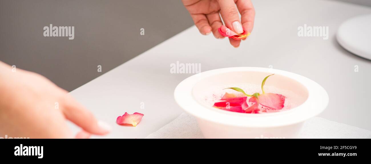 Die weiblichen Hände der Kosmetikerin bereiten das Maniküre-Bad mit Rot und Rosa vor rosenblüten auf dem Tisch im Spa Stockfoto