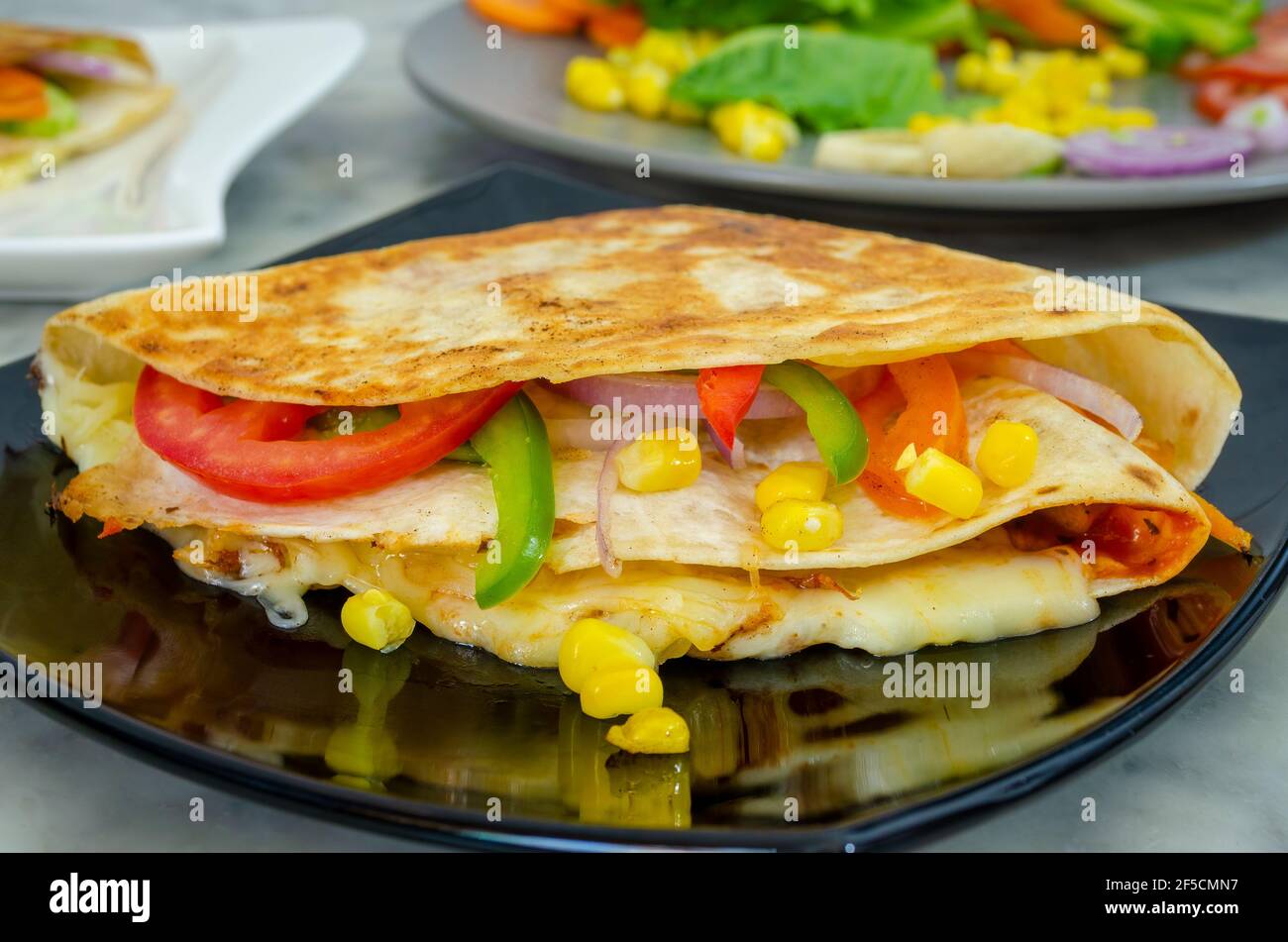 Nahaufnahme von köstlichen Tortilla Wrap Sandwich mit Gemüse und Käse In einer schwarzen Platte Stockfoto