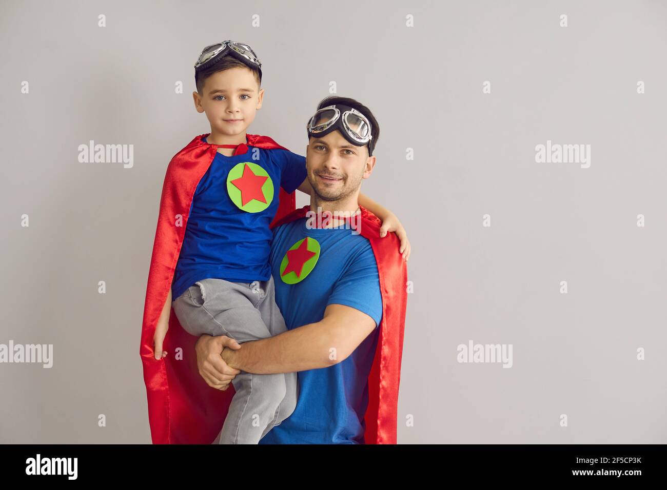 Porträt von Vater und Sohn als Superhelden gekleidet stehen in studio mit grauem Hintergrund Stockfoto