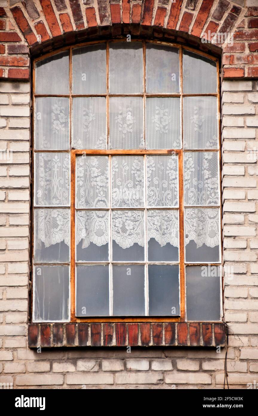 Alte rote Ziegelsteinfenster mit weißen Vorhängen Stockfoto