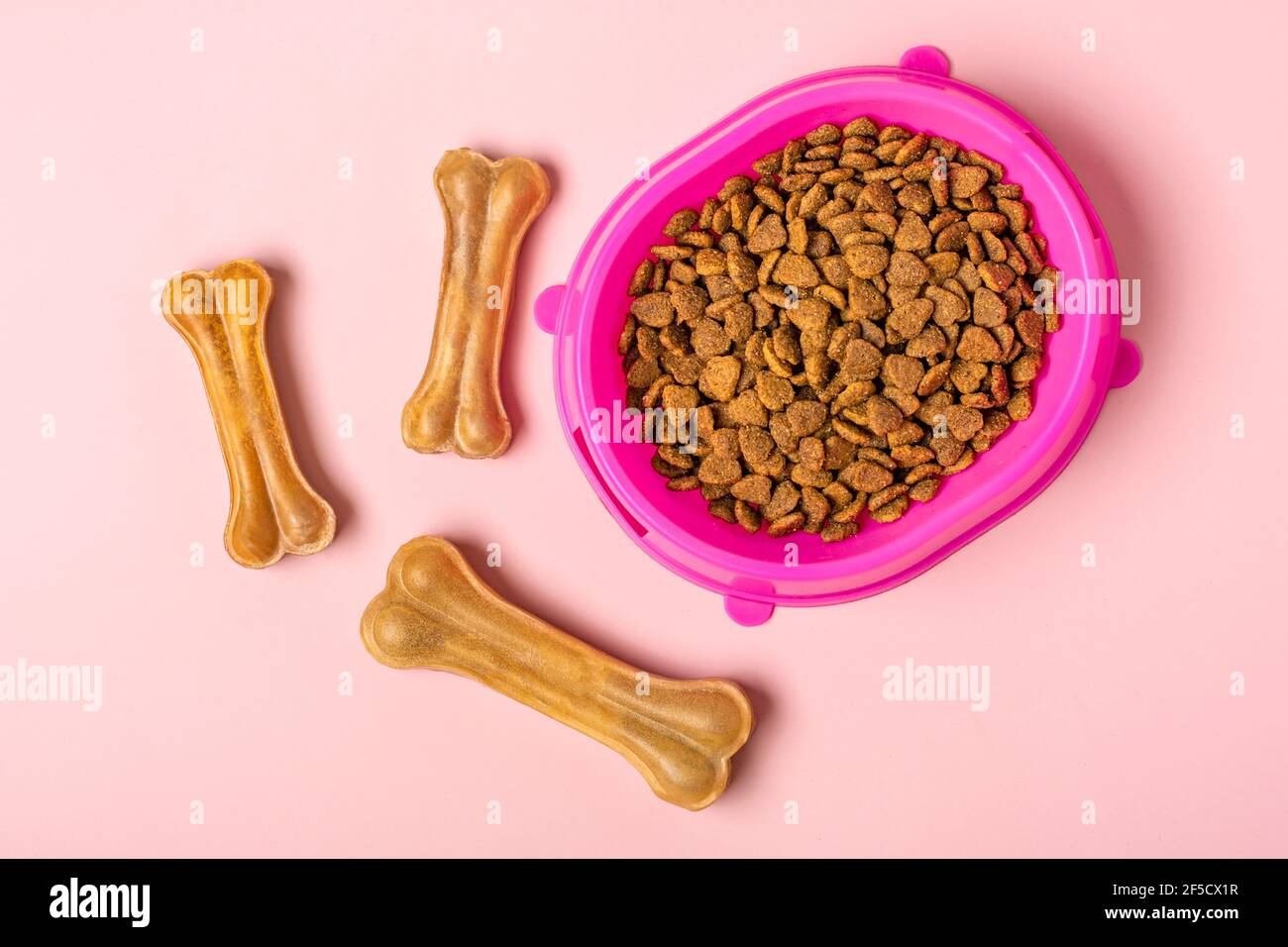 Natürliche Zahnknochen für Hund, trockene Stücke Katze oder Welpenfutter in rosa Kunststoffschale isoliert auf rosa Hintergrund Draufsicht Flat Lay Delicious Leckerbissen für Ihre Stockfoto
