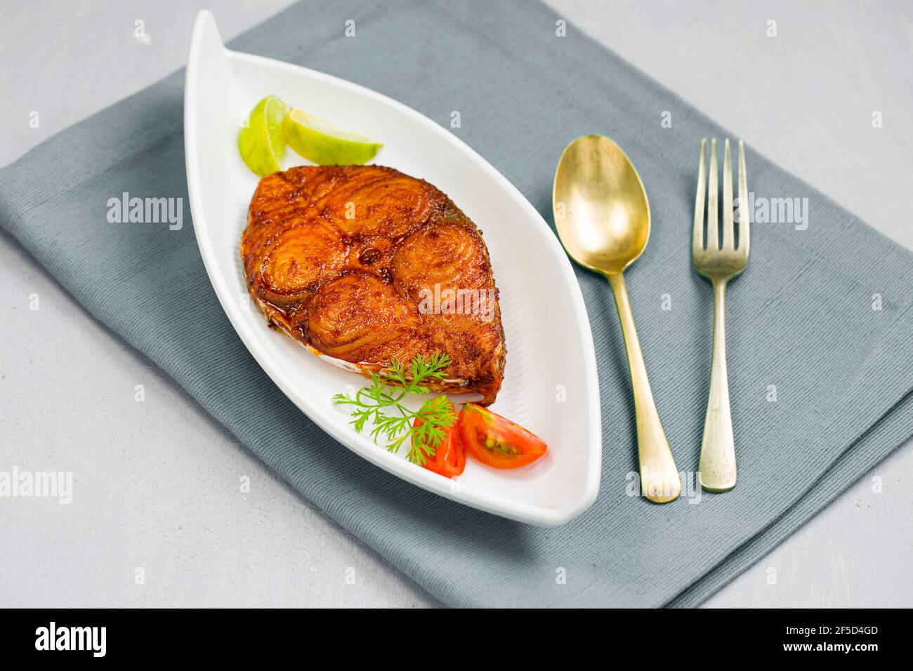 Seer Fish Fry schön arrangiert und garniert mit Zwiebel, Zitrone und Tomatenscheiben auf weißem Keramikplatte platziert auf hellen Grünschatten Servietten mit gr Stockfoto