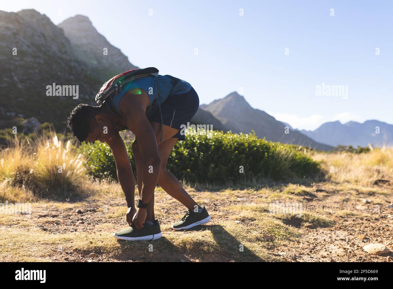 Afroamerikanischer Mann, der im Freien trainiert und Schuhe auf dem Land bindet Ein Berg Stockfoto