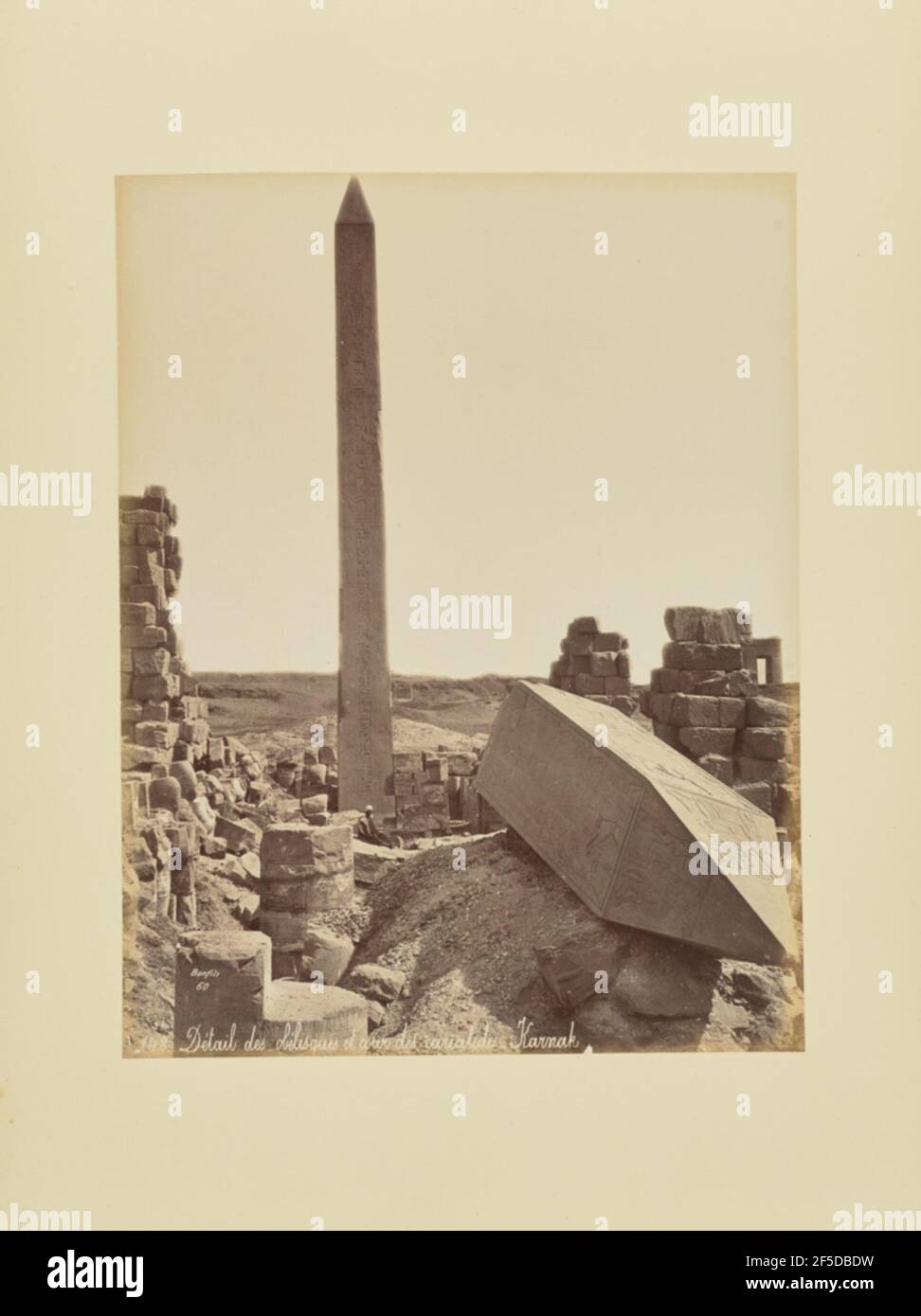 Détail des obélisques et cour des cariatides - Karnak. Blick auf die Ruinen einer Steinanlage mit dem oberen Teil eines gestürzten Obelisken im Vordergrund. Ein anderer Obelisk steht in Richtung Hintergrund, mit einem einheimischen Mann, der in der Nähe seiner Basis sitzt. (Recto, Druck) unten links, im Negativ eingeschrieben: '60 / 148   DÈtail des obÈlisques et cour des cariatides   Karnak'; Stockfoto