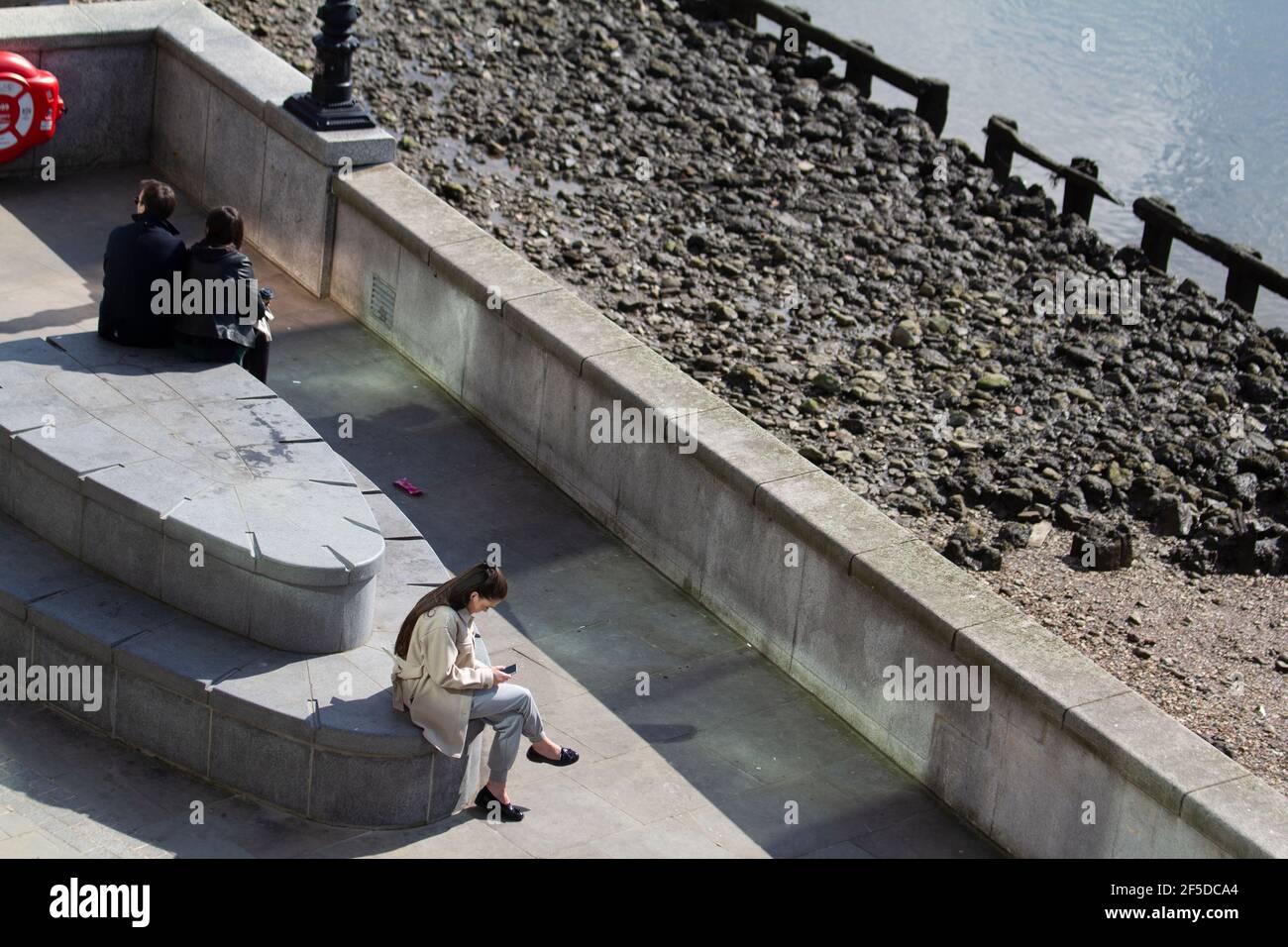 Junge Frau, die auf das Mobiltelefon am Nordufer schaut Der Themse Stockfoto