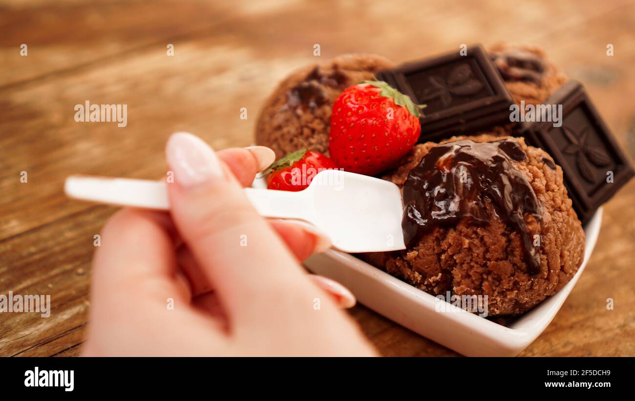 Hand mit einem Löffel. Hausgemachtes Schokoladeneis mit Schokolade und Erdbeeren Stockfoto