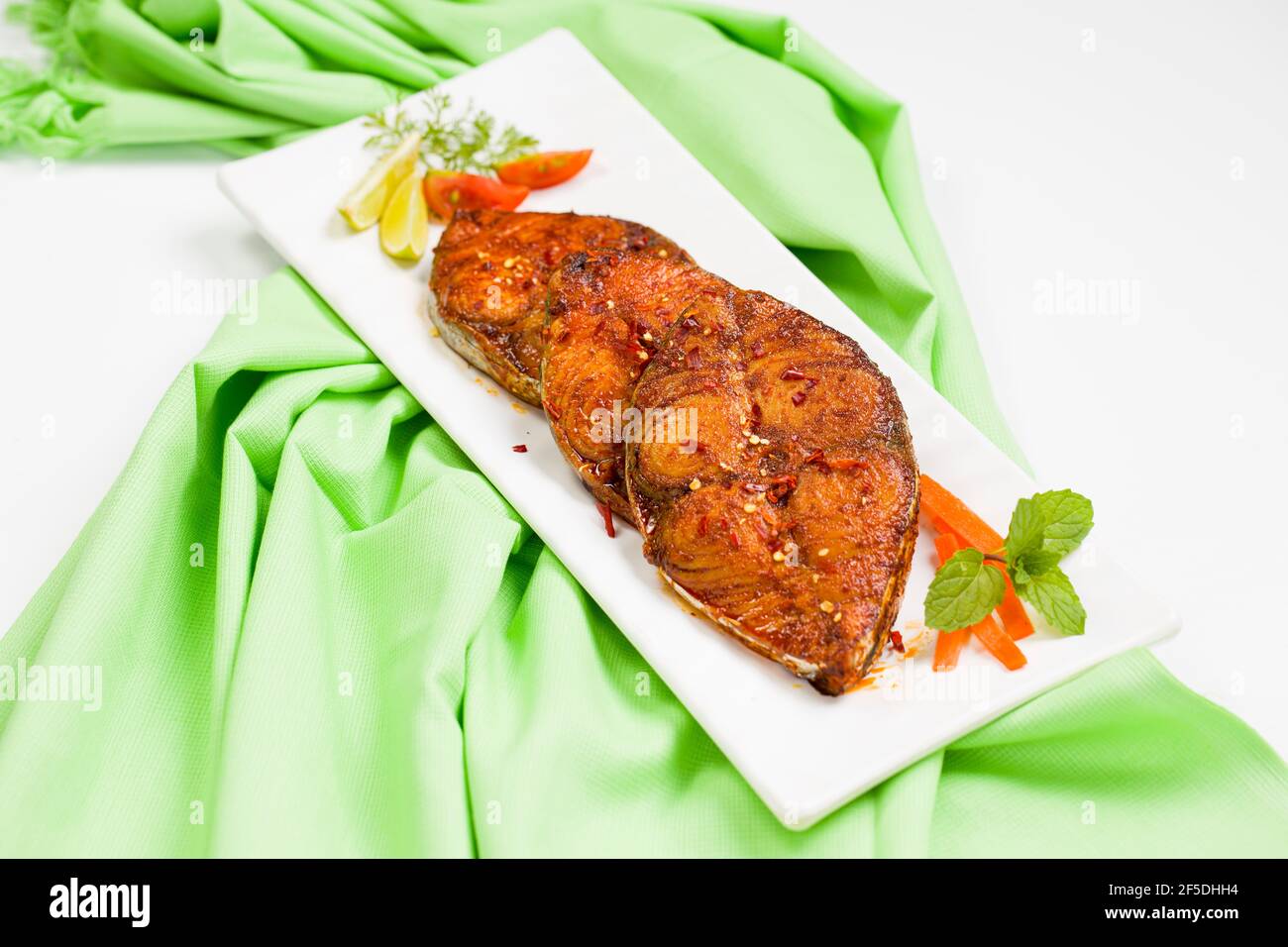 Seer Fisch braten schön angeordnet und garniert mit Zwiebeln, Zitronen-und Tomatenscheiben auf weißen rechteckigen Form Keramikplatte auf Pista grünen Colo platziert Stockfoto