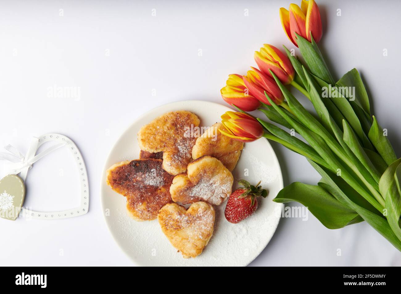 Herzen neben einem Teller mit herzförmigen Käsekuchen und Ein Bouquet von Tulpen Stockfoto