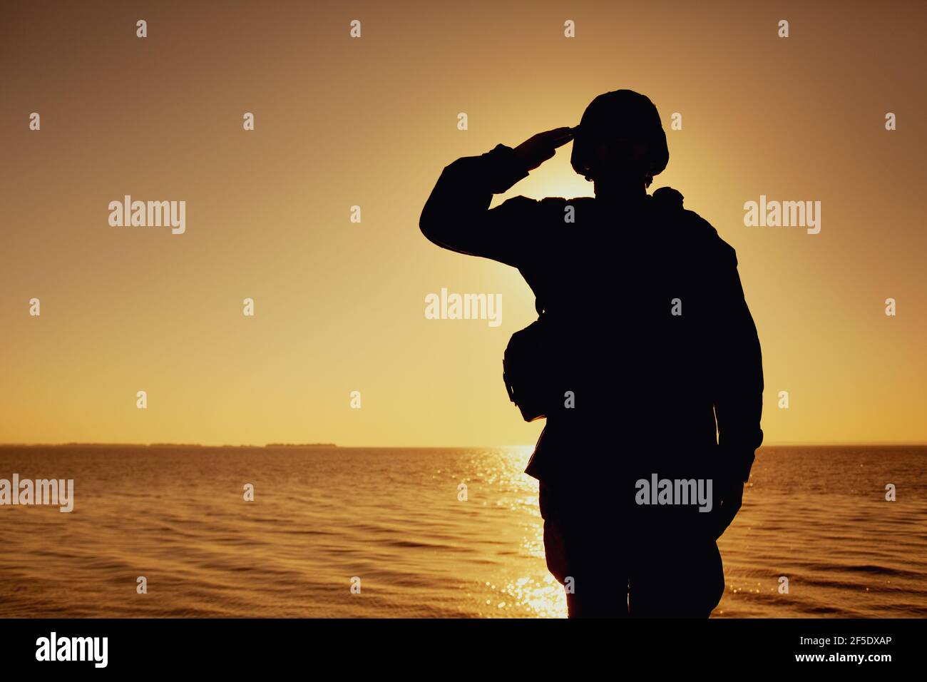 Die Silhouette des Soldaten im Kampfhelm und die Munition, die auf dem Hintergrund des Sonnenuntergangs grüßen. Armee Spezialeinheiten Kämpfer, Marines Rifleman zeigt Respekt, Begrüßung Offizier mit Gruß Geste Stockfoto