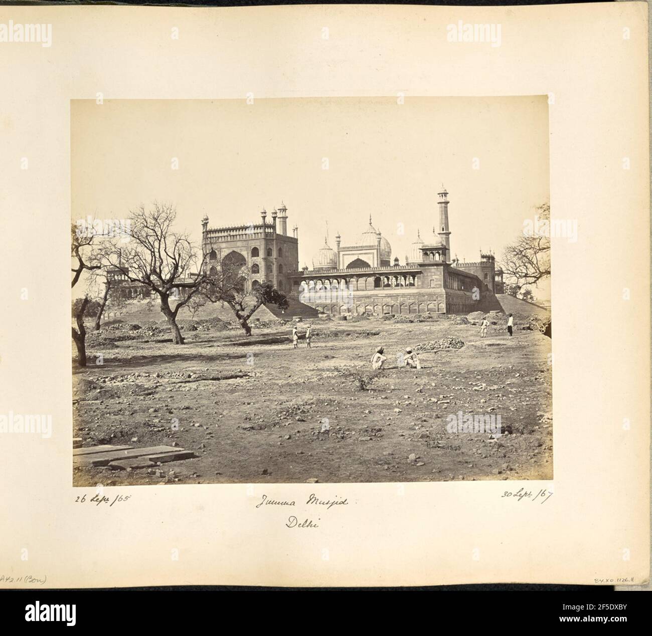 Delhi; die Jumma Musjid, aus dem Nordosten. Blick auf die Jama Masjid von Delhi von über das Land rund um das sekundäre Torhaus. Das Torhaus ist mit Iwans dekoriert, und eine Reihe von großen pyramidenförmigen Treppen führt bis zur Vorderseite des Torhauses. An den Rändern des Hofes der Moschee verläuft ein Kreuzgang mit geschwungene Bögen, eine Attika und Kuppeln an jeder Ecke. Im Hintergrund sind die Kuppeln und Minarette der Moschee zu sehen. Mehrere Männer können über das Land rund um die Moschee gesehen werden.. (Recto, Bild) unten rechts, im Negativ handgeschrieben: '1353' (Recto, Mount) lowe Stockfoto Delhi; die Jumma Musjid, aus dem Nordosten. Blick auf die Jama Masjid von Delhi von über das Land rund um das sekundäre Torhaus. Das Torhaus ist mit Iwans dekoriert, und eine Reihe von großen pyramidenförmigen Treppen führt bis zur Vorderseite des Torhauses. An den Rändern des Hofes der Moschee verläuft ein Kreuzgang mit geschwungene Bögen, eine Attika und Kuppeln an jeder Ecke. Im Hintergrund sind die Kuppeln und Minarette der Moschee zu sehen. Mehrere Männer können über das Land rund um die Moschee gesehen werden.. (Recto, Bild) unten rechts, im Negativ handgeschrieben: '1353' (Recto, Mount) lowe Stockfoto