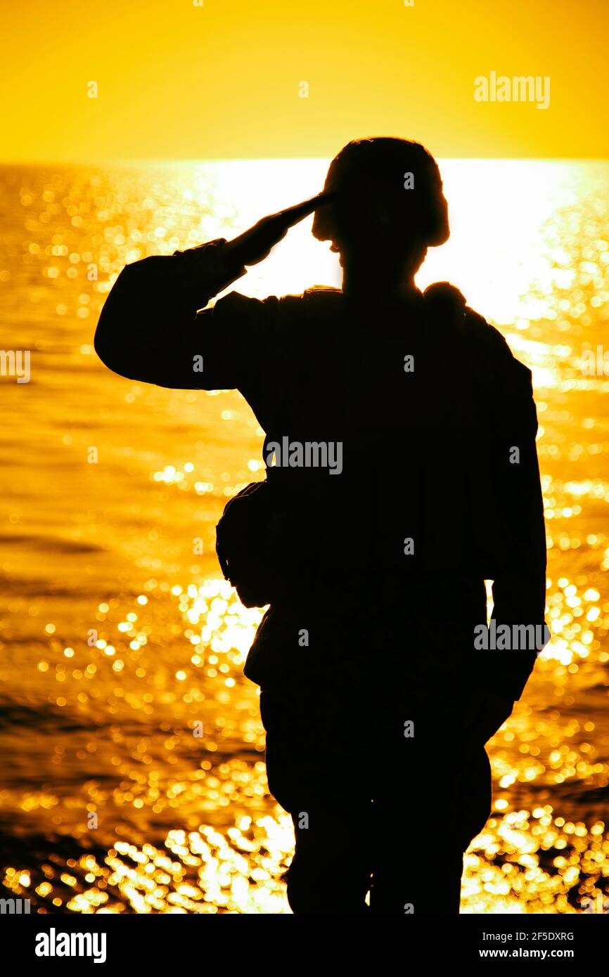 Die Silhouette des Soldaten im Kampfhelm und die Munition, die auf dem Hintergrund des Sonnenuntergangs grüßen. Armee Spezialeinheiten Kämpfer, Marines Rifleman zeigt Respekt, Begrüßung Offizier mit Gruß Geste Stockfoto