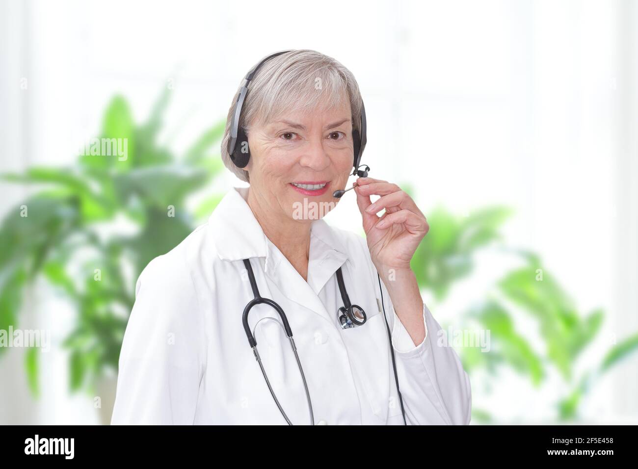 Freundlicher Oberarzt während einer Online-Konsultation, wie durch eine Webcam gesehen, heller Hintergrund. Stockfoto