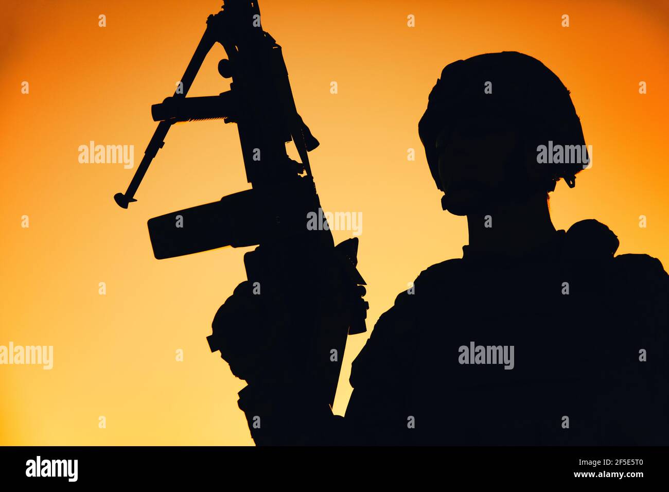 Schulter Silhouette der Armee Maschinenpistole, spezielle Operationen Kräfte Infanteristen stehend mit erhobener Waffe auf dem Hintergrund des Sonnenuntergangs Himmel. Marine Corps Shooter im Kampf Helm hält Waffe bei Sonnenaufgang Stockfoto