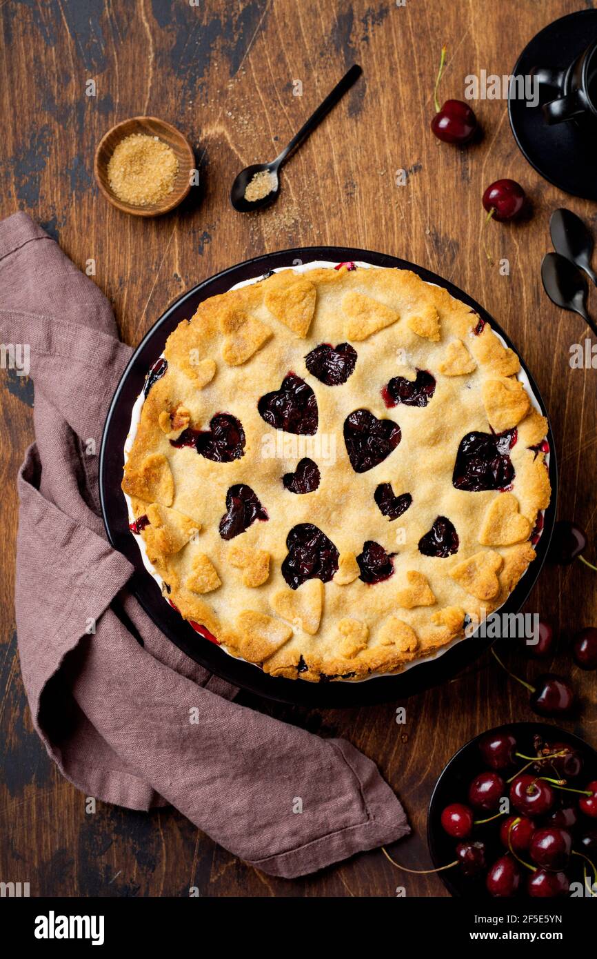 Kirschkuchen lecker hausgemacht mit Herzen auf Holzhintergrund. Valentinstag Backwaren. Draufsicht Stockfoto
