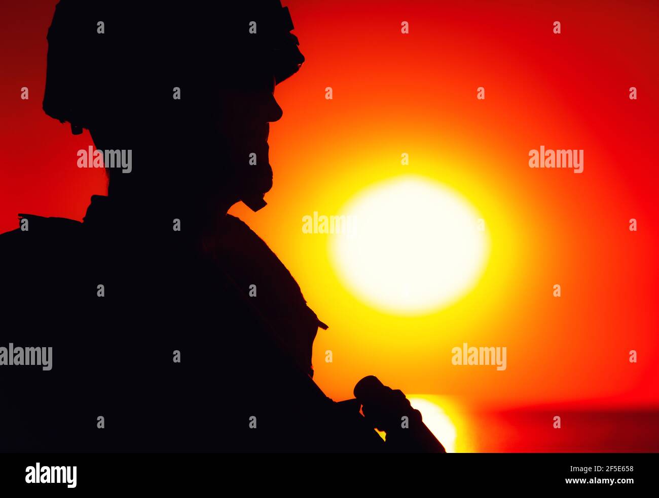 Schulter Silhouette der Armee Soldat, spezielle Operationen Kräfte Kämpfer in Kampfhelm und ballistische Brille, stehend mit Pistole auf dem Hintergrund der Untersetzung unter Ozean Horizont Sonne Stockfoto