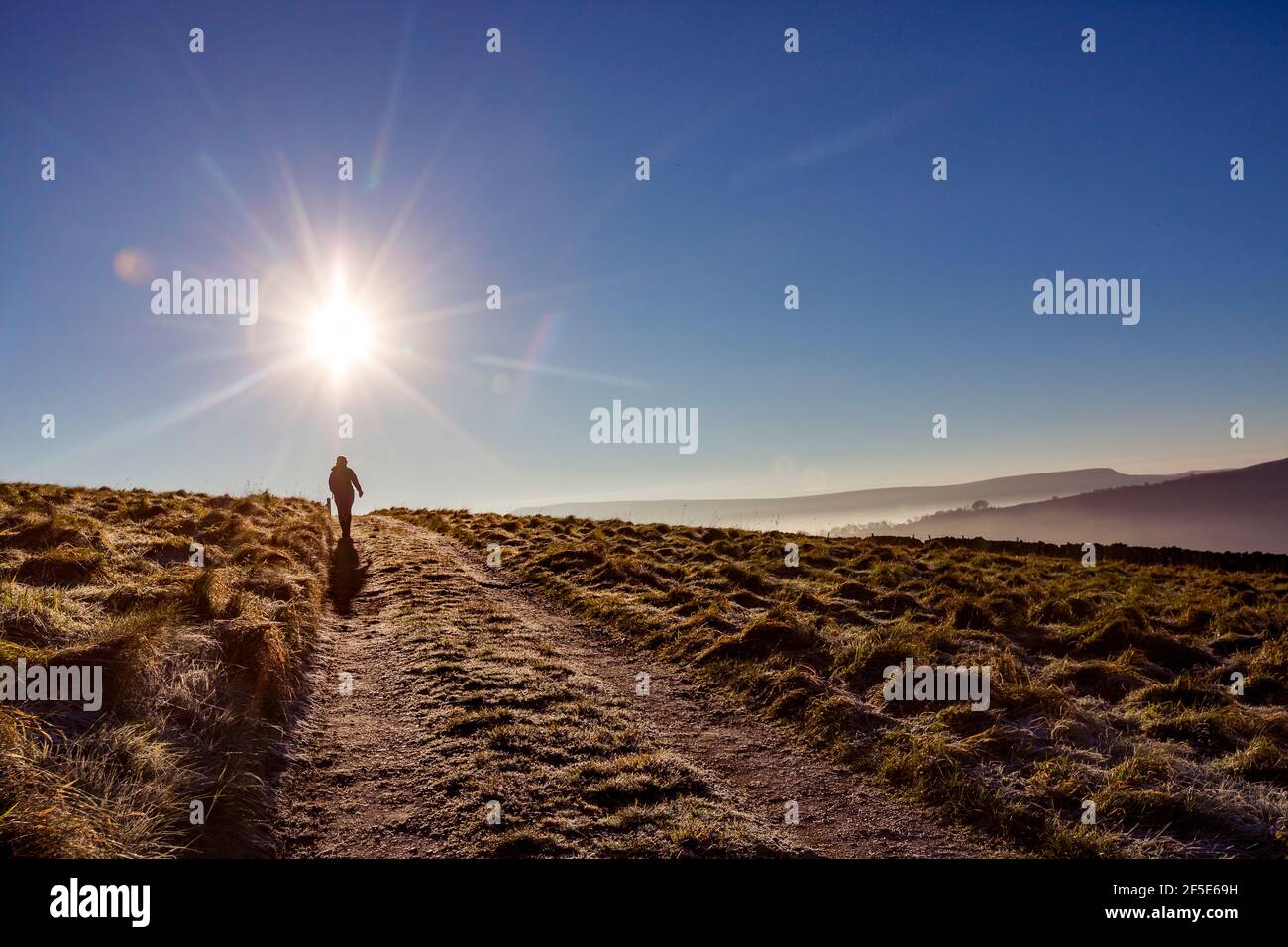 Frau Silhouetten gegen die helle Sonne zu Fuß auf einer Spur in der High Peak, Derbyshire, Großbritannien Stockfoto