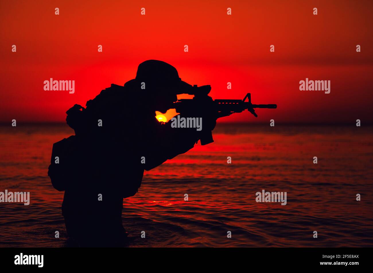 Silhouette der Armee Soldat zielen und schießen Service Gewehr während knietief im Meerwasser stehen. Küstenwache, Seestreitssoldat, der den Feind mit Waffen angreift, Landung am Strand bei Sonnenuntergang oder Morgendämmerung Stockfoto