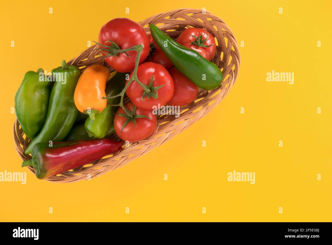 Lange Paprika und Tomaten in einem Weidenkorb. Isoliert auf gelbem Hintergrund.Kopiebereich der Draufsicht Stockfoto
