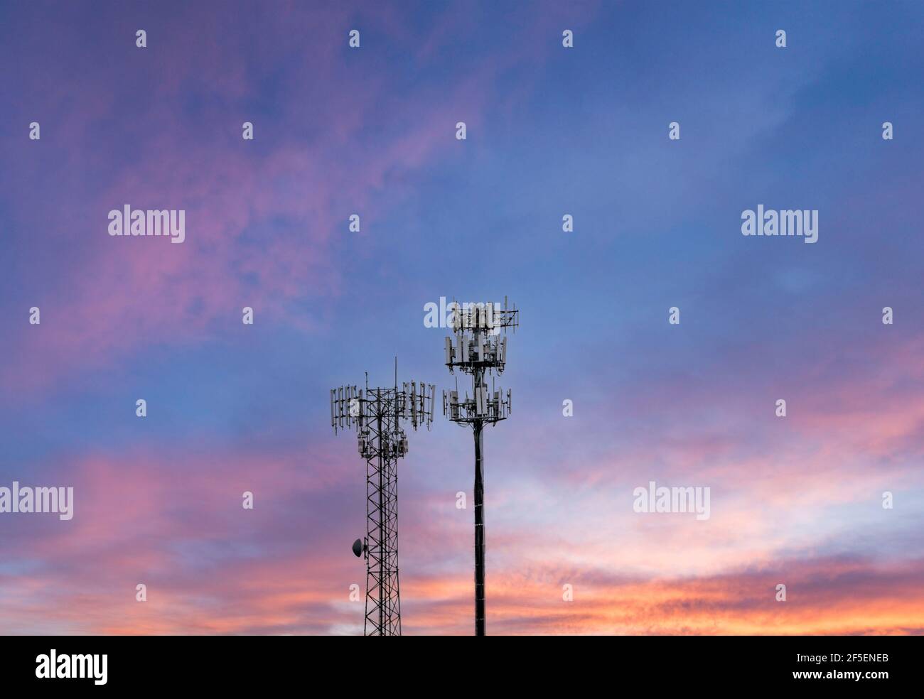 Zwei Türme, die gegen Sonnenuntergang zelluläre Breitband- und Datendienste für ländliche Gebiete bereitstellen. Zeigt die digitale Teilung. Stockfoto