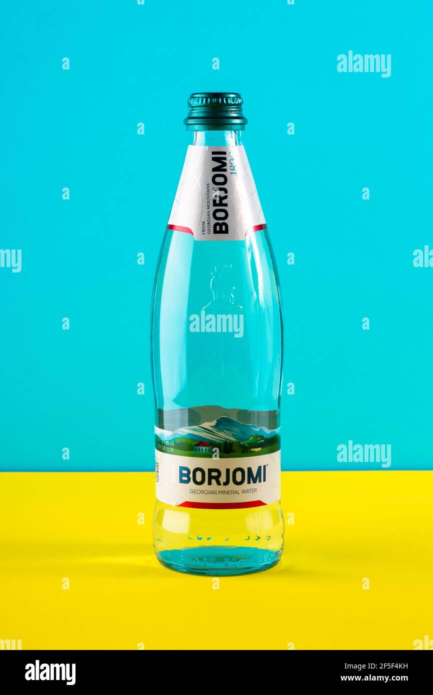 Borjomi Glasflasche auf gelbem und blauem Papierhintergrund. Logo, Marke des Unternehmens. Georgische Mineralwasser, durstlöschende Getränk, das h beseitigt Stockfoto